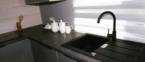 A modern kitchen with a black sink, white teapots, and a wooden spatula on the counter.