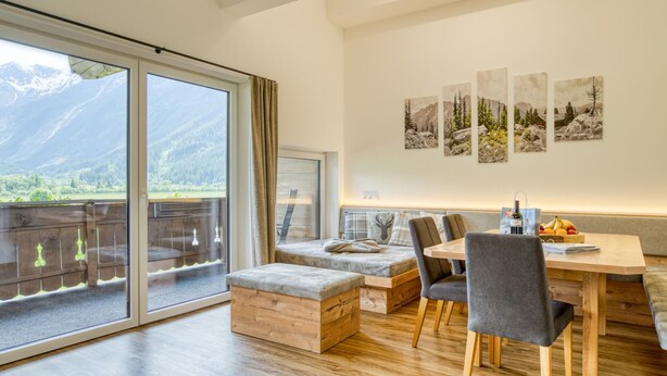 A modern living room with a wooden floor, a dining table with chairs, a sofa, and a balcony with a mountain view. - Chalet in Neukirchen With Mountain Views (Neukirchen am Grossvenediger)