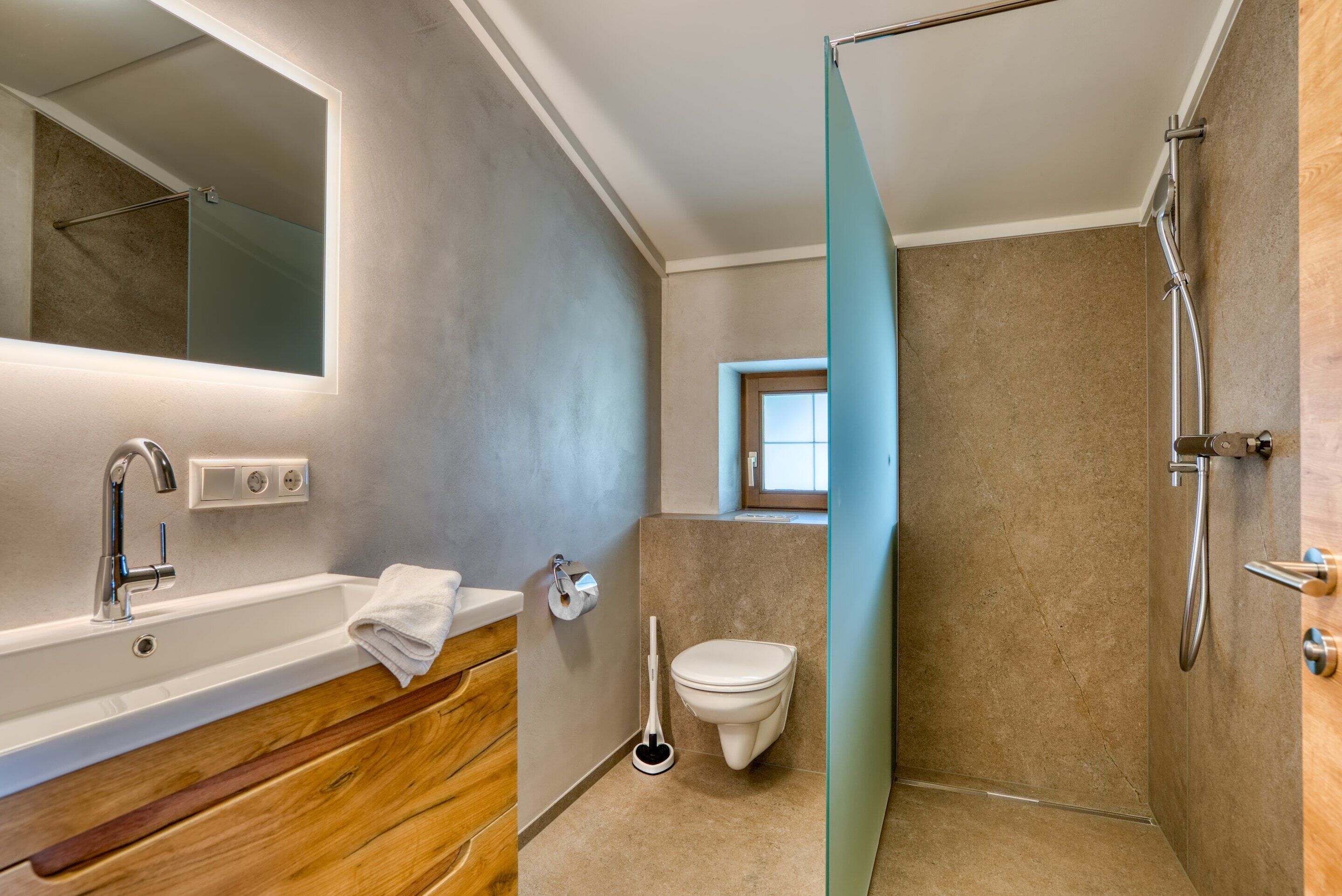 A modern bathroom with a wooden vanity, a white sink, a glass shower enclosure, and a toilet.