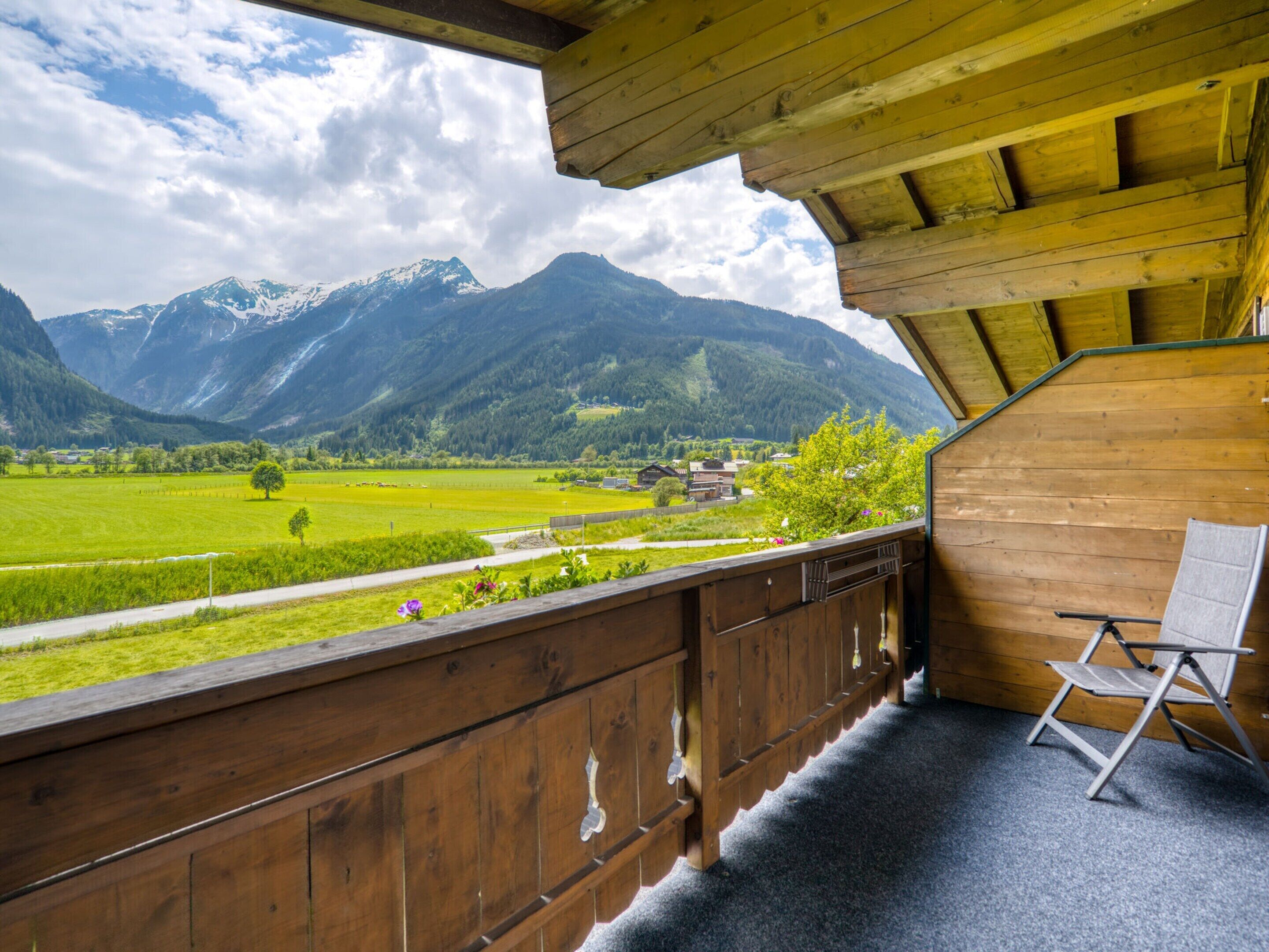 A wooden balcony with a view of a green valley and mountains.