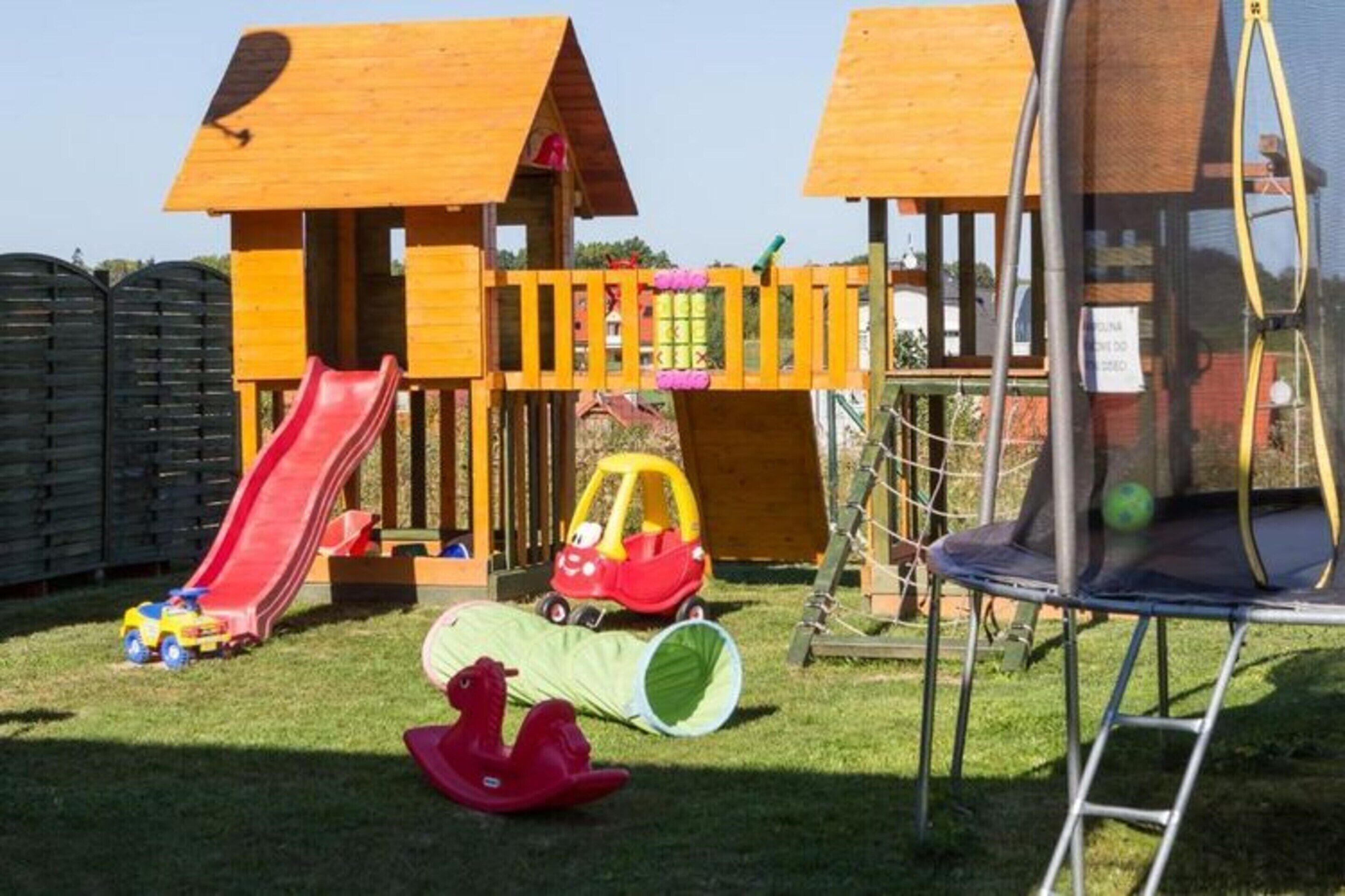 A playground with a slide, a small car, and a trampoline.