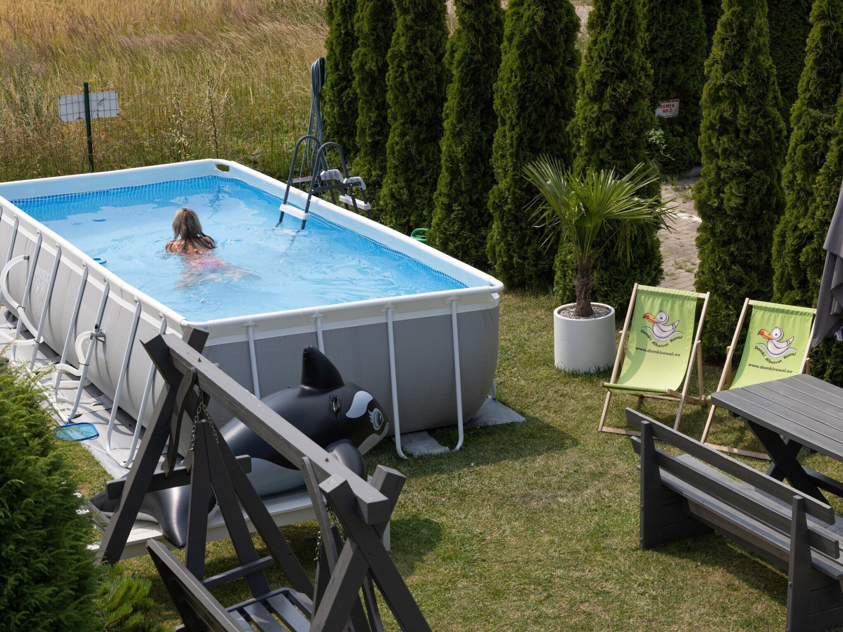 Une piscine hors sol, équipée d’une échelle, entourée de pelouse et d’arbres.