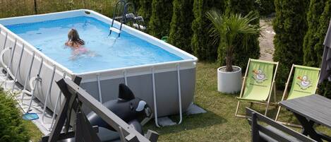 An above-ground swimming pool with a ladder, surrounded by grass and trees.