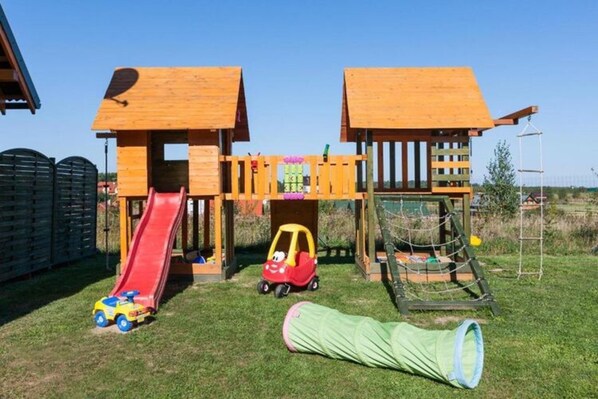 A wooden play structure with a slide and climbing area, surrounded by a grassy yard. - Terraced House in Rewal Near Sandy Beach (Rewal)