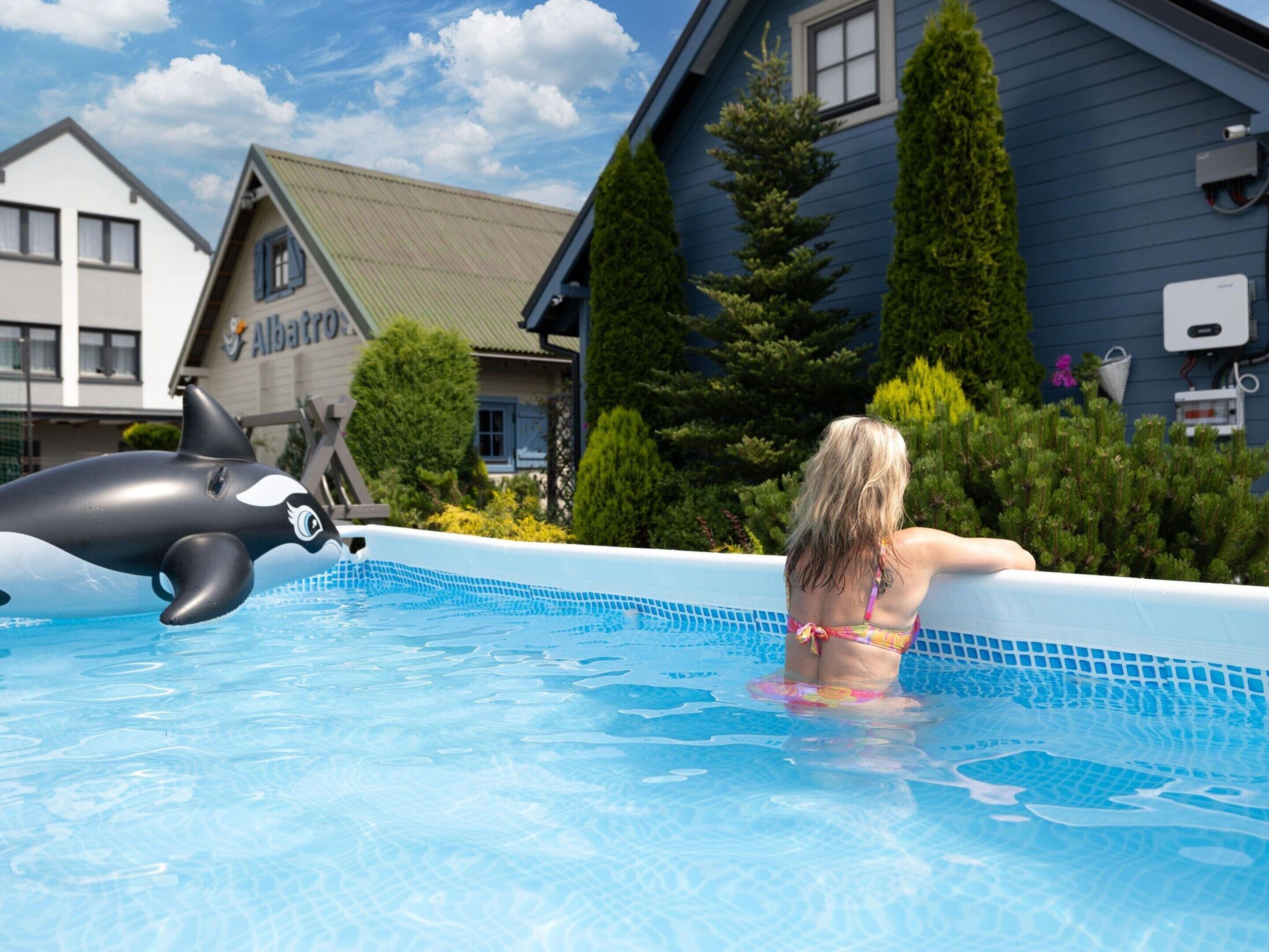 A swimming pool with a dolphin floatation device, a person in a bikini, and a building with a sign that reads "Albatros".