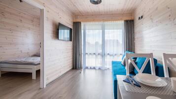 A room with a bed, a TV mounted on the wall, a dining table with chairs, and a view of the outdoors through a window.