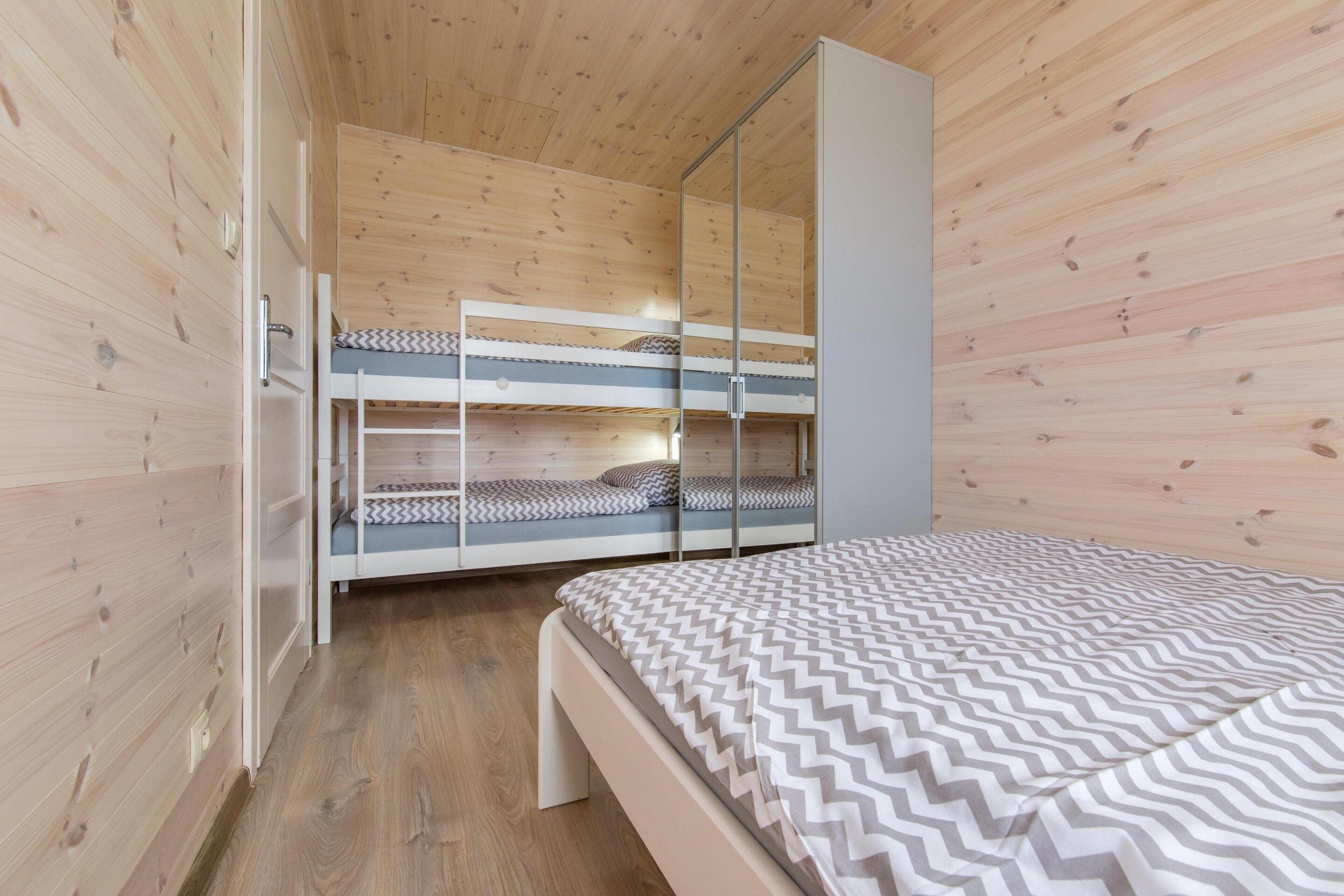 Una habitación con literas, un armario y una cama con cubrecama estampado.