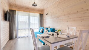 Una camera moderna e luminosa con un tavolo da pranzo per quattro, un divano con cuscini blu e un'ampia finestra con tende leggere.