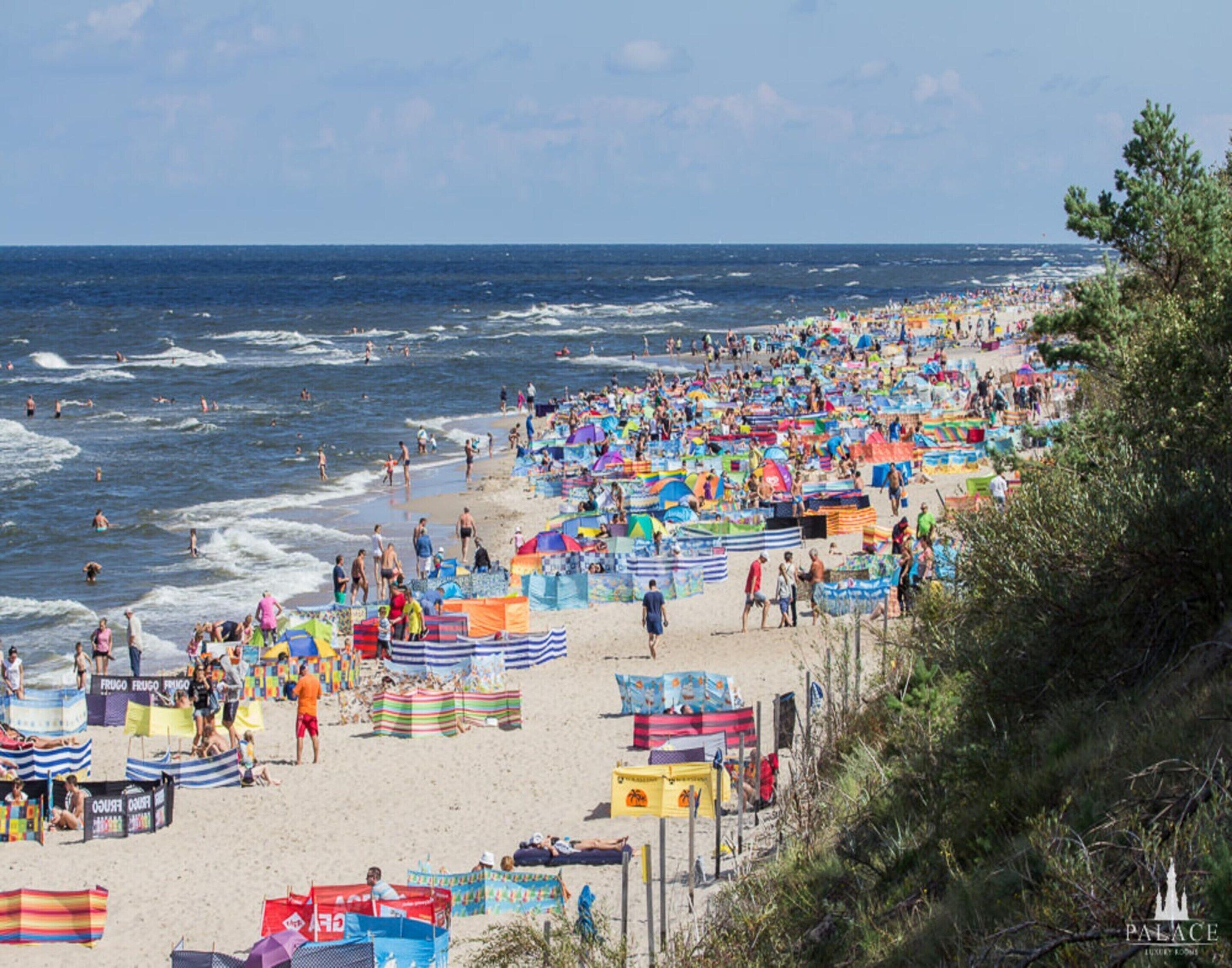 Una playa concurrida, con numerosos paraguas de colores y gente.
