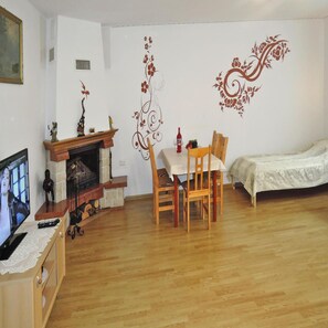 A living room with a fireplace, a dining table with chairs, a bed, and a television on a wooden cabinet. - Holiday Home in Kolczewo Near Baltic Sea (gmina Wolin)
