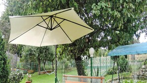 Un patio al aire libre con una mesa y bancos de madera, un paraguas grande y un estanque pequeño con nenúfares.