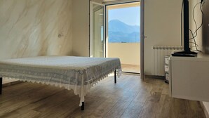 A bedroom with a bed, a television on a stand, and a view of mountains through an open door. - Holiday Home Casa Simone in Lido (Camaiore)