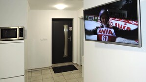 A hallway with a microwave, a refrigerator, a door with a doormat, and a television displaying a sports event. - Holiday Flat in Kolczewo-70 qm for 6 Persons (gmina Wolin)