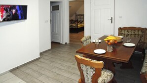 A dining area with a wooden table set for four, chairs with floral upholstery, a television mounted on the wall, and a door leading to a bedroom with a bed. - Holiday Flat in Kolczewo-70 qm for 6 Persons (gmina Wolin)