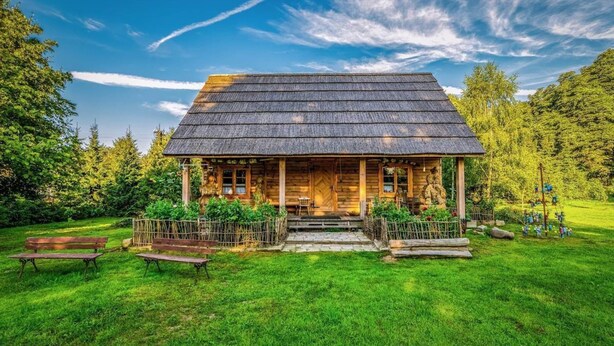 A rustic wooden cabin with a thatched roof, surrounded by a well-maintained lawn and trees. - Holiday Home in Belczna Near Klepnicko Lake (Łobez)
