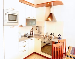 Una cocina compacta con gabinetes blancos, microondas, estufa y pileta.