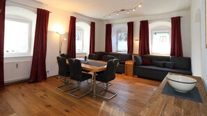 A modern living room with a wooden dining table, black chairs, a grey sofa, and red curtains. - Apartment in Fugen Near Spieljochbahn (Fuegen)