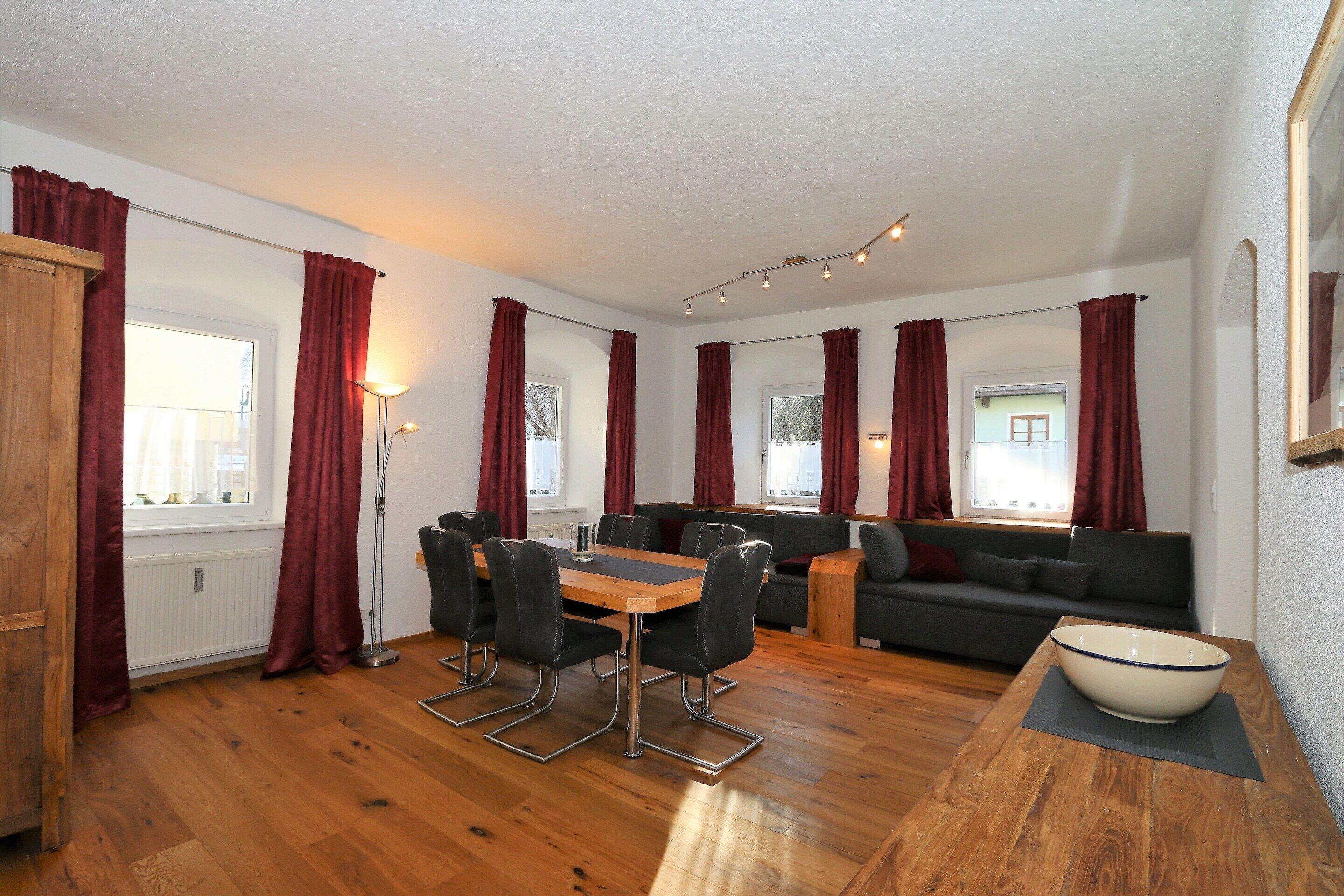 Una habitación con una mesa de comedor de madera, sillas negras, un sofá y un cuenco blanco grande sobre un tapete.