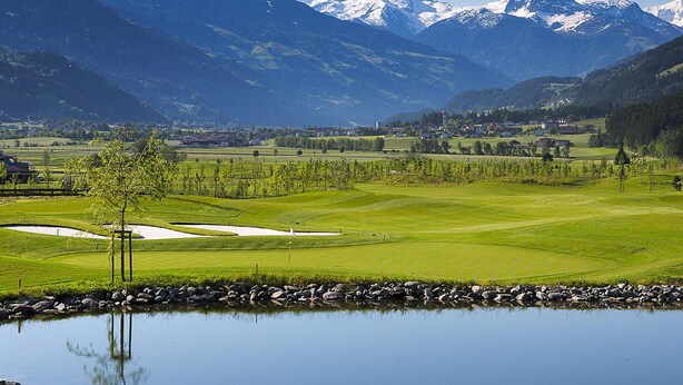 A golf course with a pond, trees, and mountains in the background. - Apartment in Fugen Near Spieljochbahn (Fuegen)