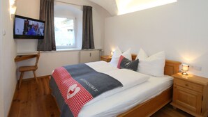 A bedroom with a bed, a TV mounted on the wall, a window with curtains, a wooden chair, and a nightstand with a lamp. - Apartment in Fugen Near Spieljochbahn (Fuegen)