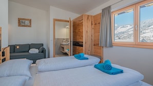 Une chambre avec deux lits, un canapé, un mur en bois, une salle de bain et une fenêtre donnant sur un paysage enneigé.