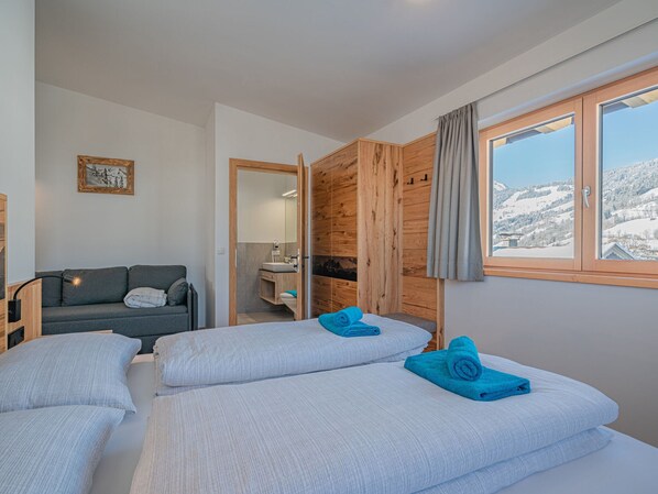 Ein Zimmer mit zwei Betten, einer Schlafcouch, einer Holzwand, einem Badezimmer und einem Fenster mit Blick auf Schnee.