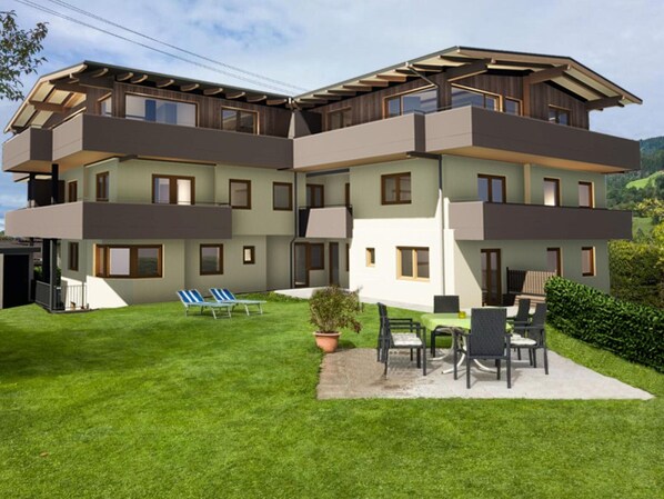 Un immeuble résidentiel à plusieurs étages, doté d’un toit plat, de balcons et d’une pelouse bien entretenue agrémentée de mobilier d’extérieur.