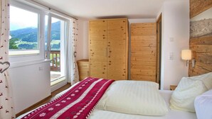 A bedroom with a bed, a window with curtains, wooden wardrobes, and a view of the outdoors. - Apartment in Hohe Tauern With Mountain Views (Neukirchen am Grossvenediger)