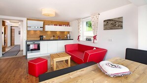 A modern kitchen with white cabinets, a red sofa, and a wooden dining table. - Apartment in Hohe Tauern With Mountain Views (Neukirchen am Grossvenediger)