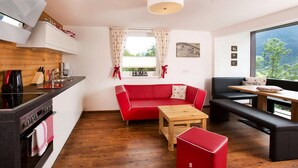 A compact living space with a kitchenette, a red sofa, a wooden table, and a bench. - Apartment in Hohe Tauern With Mountain Views (Neukirchen am Grossvenediger)