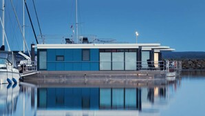 A modern building with a blue facade, large windows, and a dock area with boats. - Hausboot in Boltenhagen (Boltenhagen)
