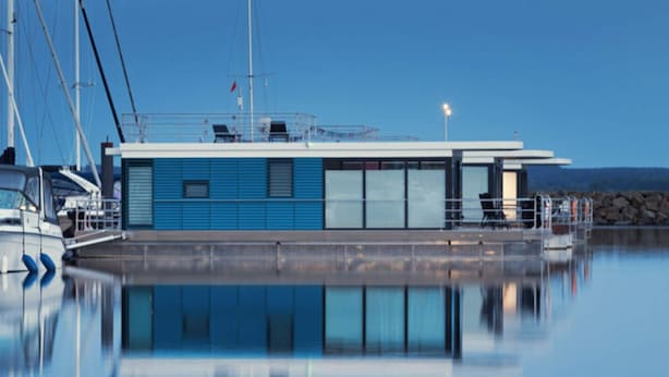 A modern building with a blue facade, large windows, and a dock area with boats. - Hausboot in Boltenhagen (Boltenhagen)
