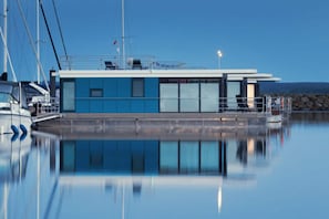 A modern building with a blue facade, large windows, and a dock area with boats. - Hausboot in Boltenhagen (Boltenhagen)