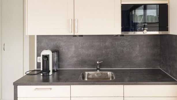 A modern kitchen with white cabinets, a black countertop, a stainless steel sink, and a coffee maker. - Hausboot in Boltenhagen (Boltenhagen)