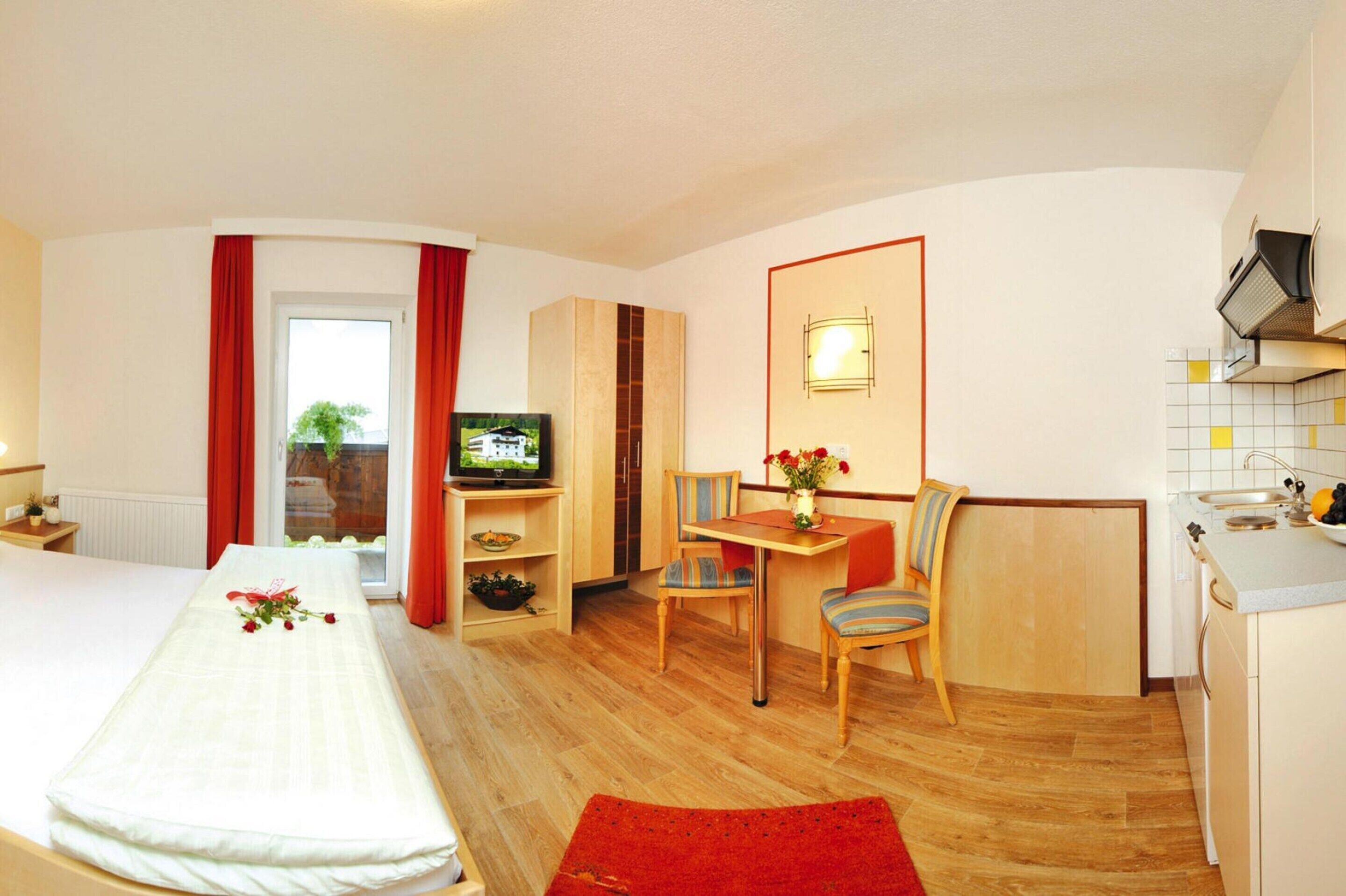 Ett hotellrum med en säng, ett skrivbord, en stol, en tv och ett litet kök.
