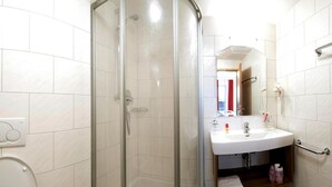 Un baño con ducha acristalada, lavabo blanco y espejo.