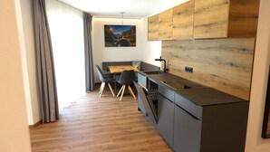A modern kitchen with a wooden backsplash, a dining area with a table and chairs, and a large window with curtains. - Bergzeit Apartments Near ski Slope (Saalbach-Hinterglemm)