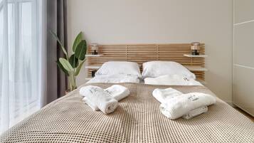 A neatly made bed with white linens and towels, a wooden headboard, and a large window with sheer curtains.
