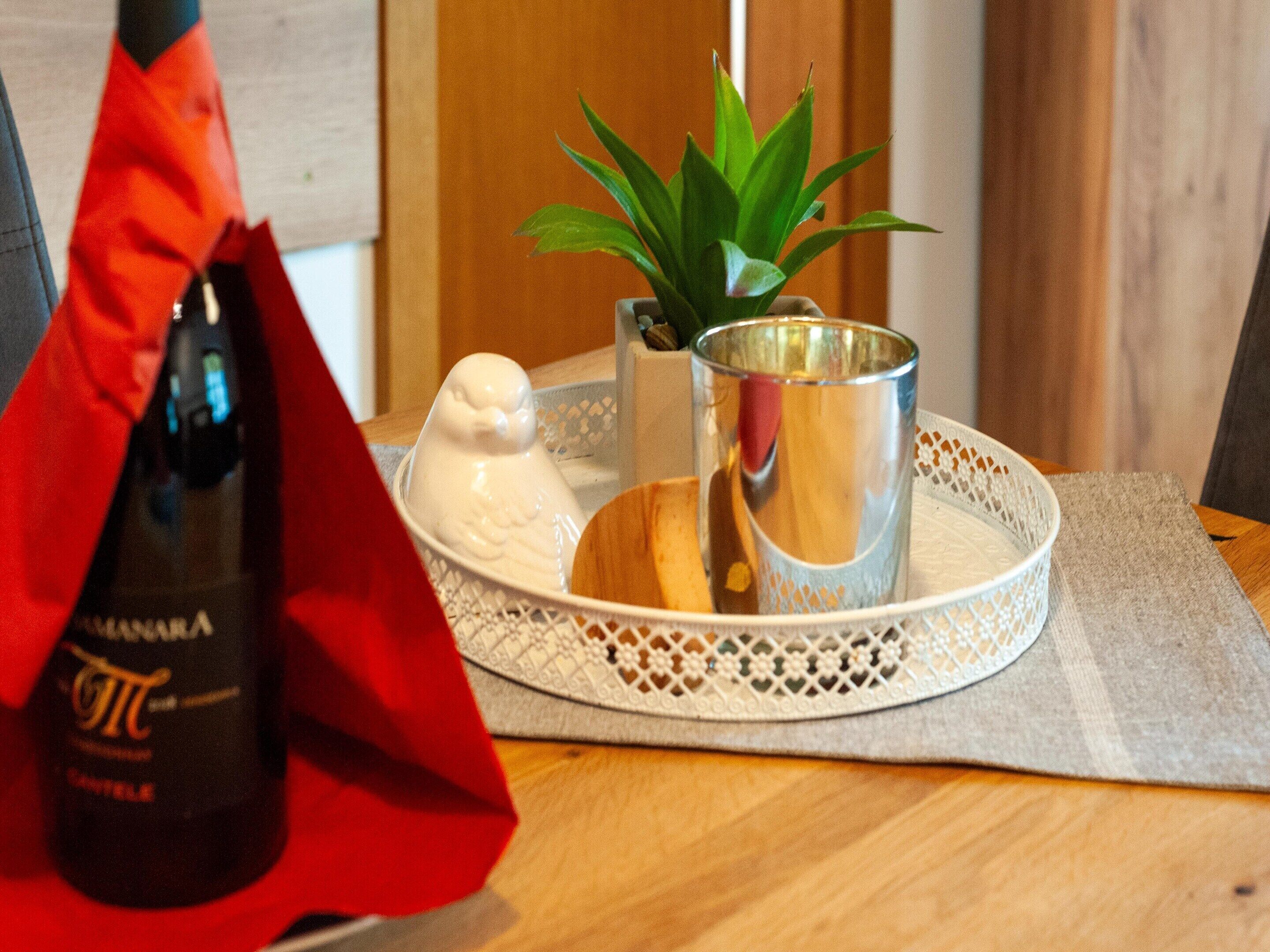 A bottle of wine, a bird-shaped salt shaker, a small potted plant, and a metal cup on a tray.