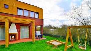 A modern house with a brick exterior, a wooden deck, a swing set, and a small garden area. - Holiday Home With a Private Garden (Mielno)