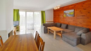 A modern living room with a wooden dining table, grey sofa, and a painting on the wooden wall. - Holiday Home With a Private Garden (Mielno)