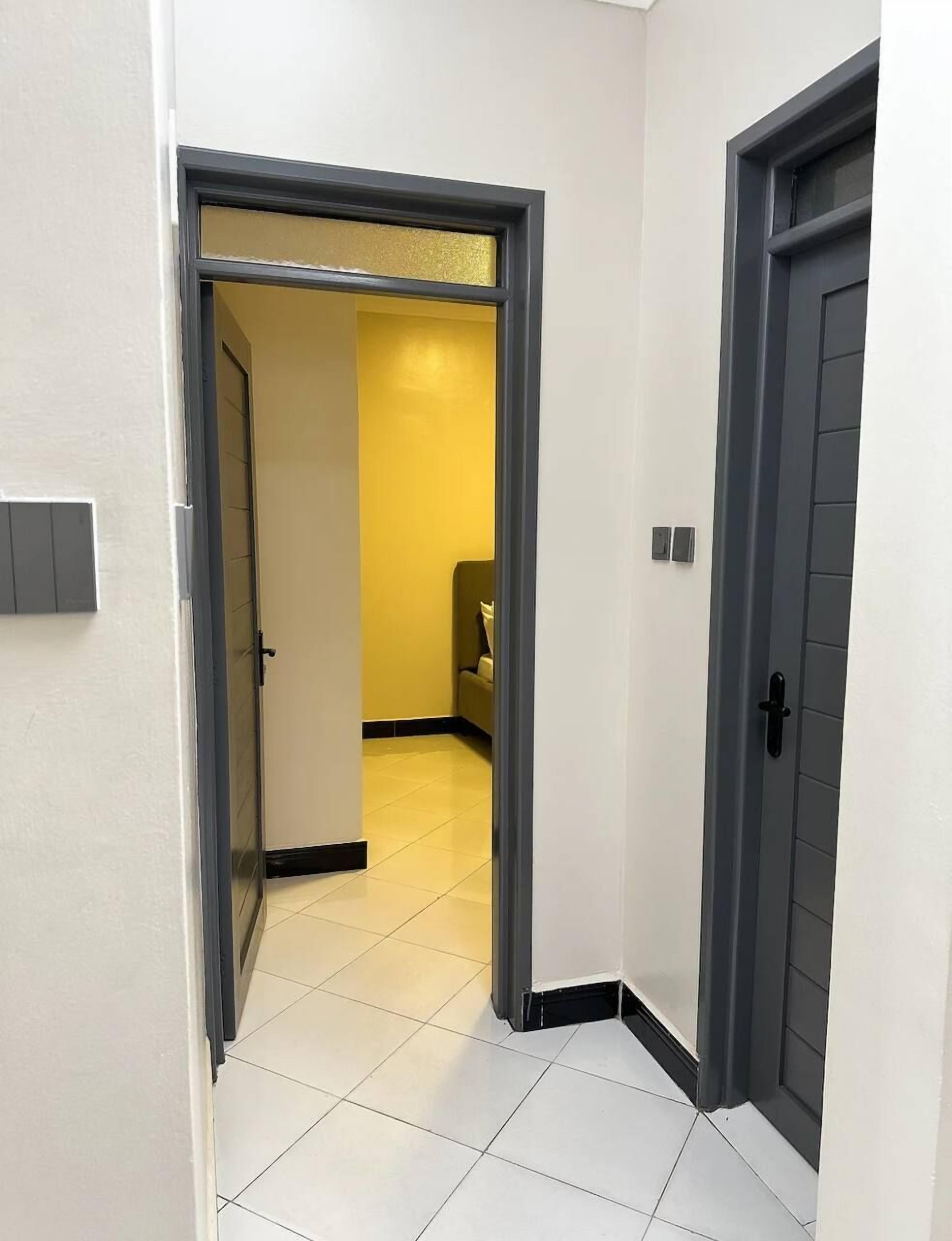 A hallway with a tiled floor, a door with a black handle, and a light switch on the wall.