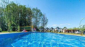A swimming pool with a clear blue water surface, surrounded by trees and a row of houses in the background. - Spacious Holiday Homes With air Conditioning, Pool (Rewal)