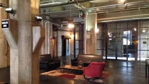 A lobby with a leather sofa, a red chair, and a coffee table. There is a sign on the wall and a large window in the background. - Luxury 1 BDR Loft: Near State Fair w/ Rooftop Pool (Dallas)