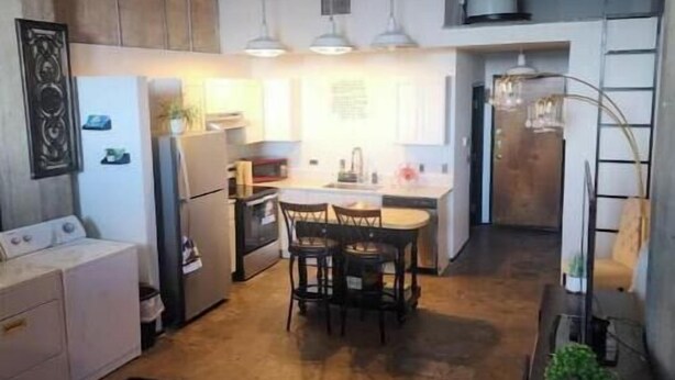 A compact kitchen with modern appliances, a dining area with a table and chairs, and a visible laundry area. - Luxury 1 BDR Loft: Near State Fair w/ Rooftop Pool (Dallas)