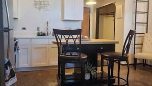 A kitchen with white cabinets, a dining table with four chairs, pendant lights, and a ladder against the wall. - Luxury 1 BDR Loft: Near State Fair w/ Rooftop Pool (Dallas)