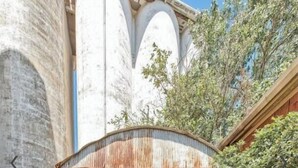 A rustic outdoor seating area with a metal roof, surrounded by a stone wall and vegetation. - Luxury 1 BDR Loft: Near State Fair w/ Rooftop Pool (Dallas)