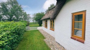 A white brick house with a thatched roof, a stone pathway, and a well-maintained hedge. - Historisches Reetdachhaus in Ruhiger Lage (Tating)