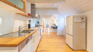 A modern kitchen with wooden cabinets, a stainless steel sink, and a white refrigerator. - Historisches Reetdachhaus in Ruhiger Lage (Tating)