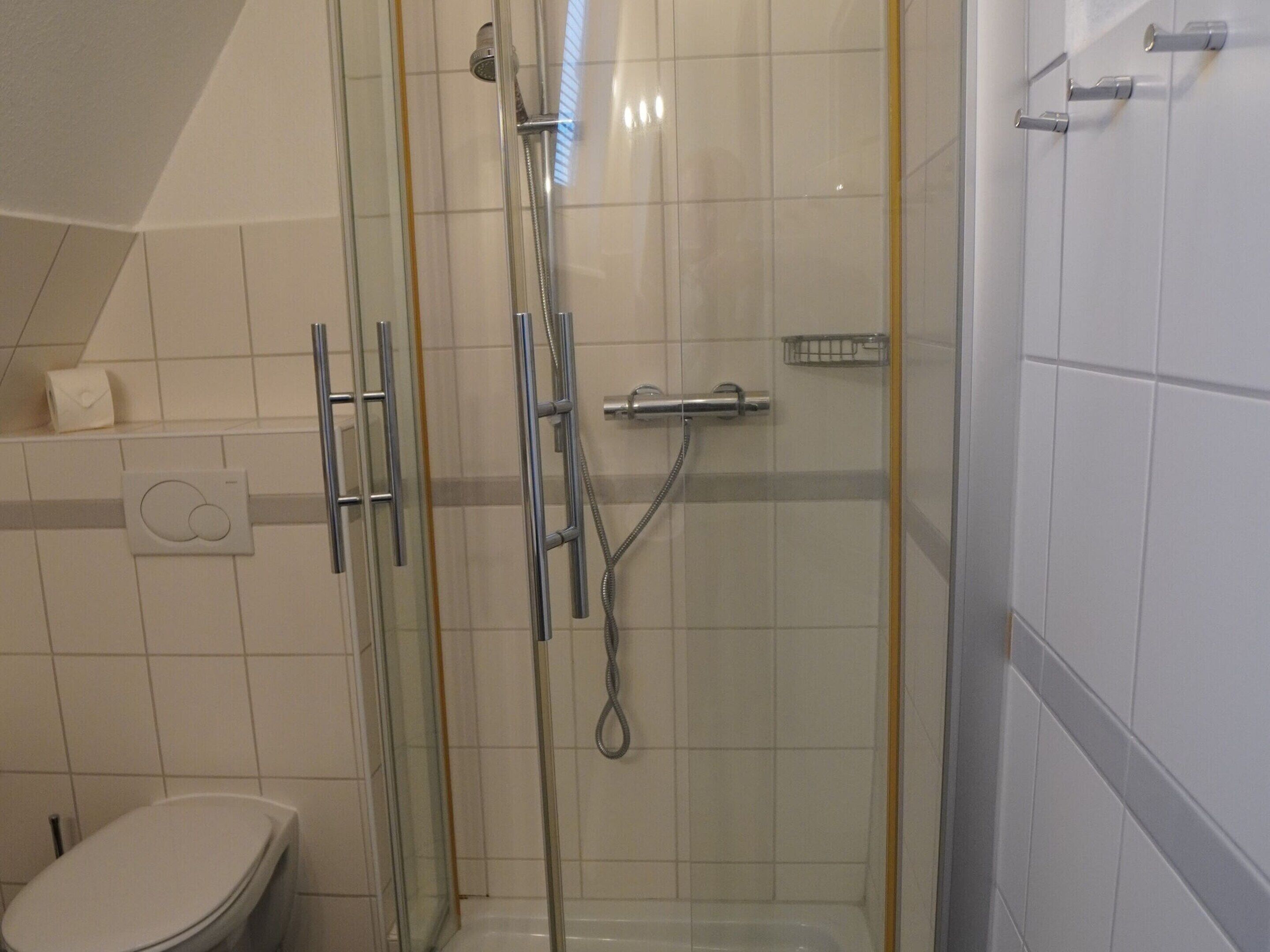 Área de chuveiro envidraçada com chuveiro manual, pulverizador manual e torneira fixada na parede.